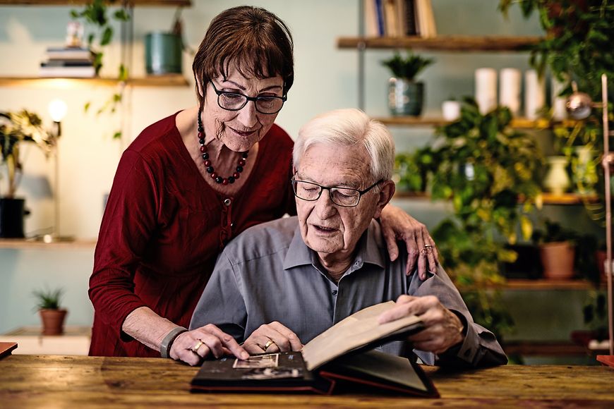 Zwei Senioren schauen sich ein Fotoalbum an. Ältere Menschen sollten jetzt möglichst alle sozialen Kontakte meiden