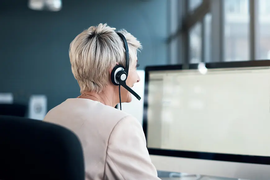 Eine Frau sitzt mit einem Headset an einem Computer