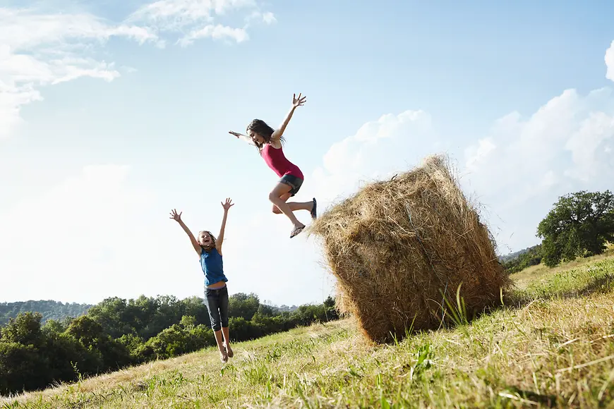 Jugendliche auf einem Feld springen von einem Heuballen