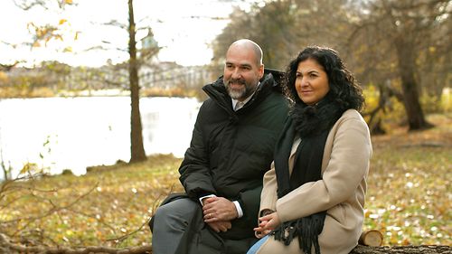 Adoptiveltern sitzen auf einer Bank in der Natur und geben ein Interview.