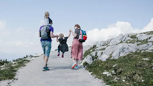 Eine Familie läuft eine Düne hinauf, ein hüpfendes Kind zwischen ihnen. Der Vater trägt ein weiteres Kind auf den Schultern.