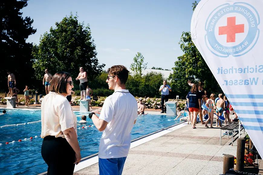 Ekin Deligöz steht vor einem Schwimmbecken im Freibad und unterhält sich mit einem Vertreter des Freibads