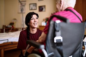 Eine junge Frau kniet vor einer älteren Frau im Rollstuhl