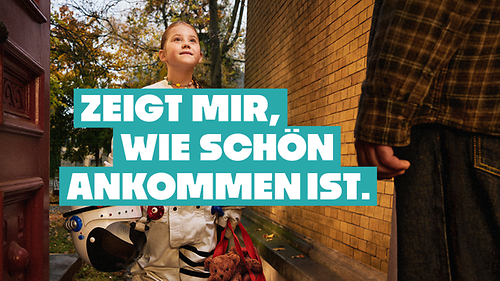 Ein Kind in einem Astronautenanzug steht vor einer geöffneten Haustür, darüber steht der Satz "Zeig mir, wie schön Ankommen ist"
