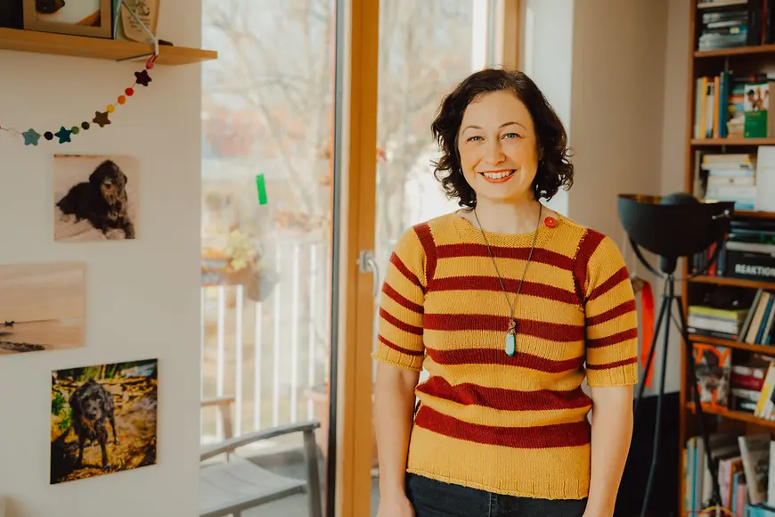 Eine junge Frau mit buntem T-Short vor Fenster und Regal