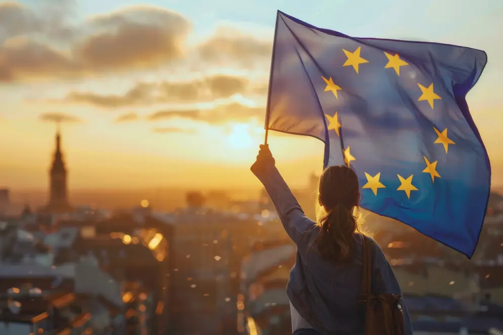 Eine Person mit langen Haaren schwenkt eine große EU-Flagge vor dem Panorama einer Stadt