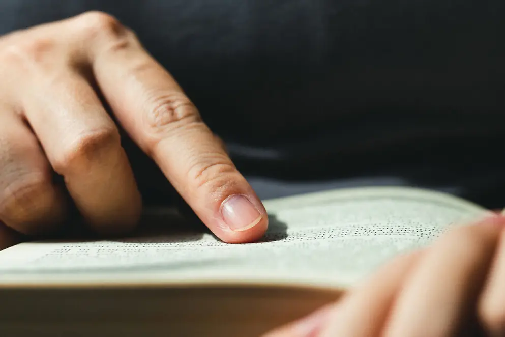 Ein Finger fährt Buchstaben auf einer Buchseite nach