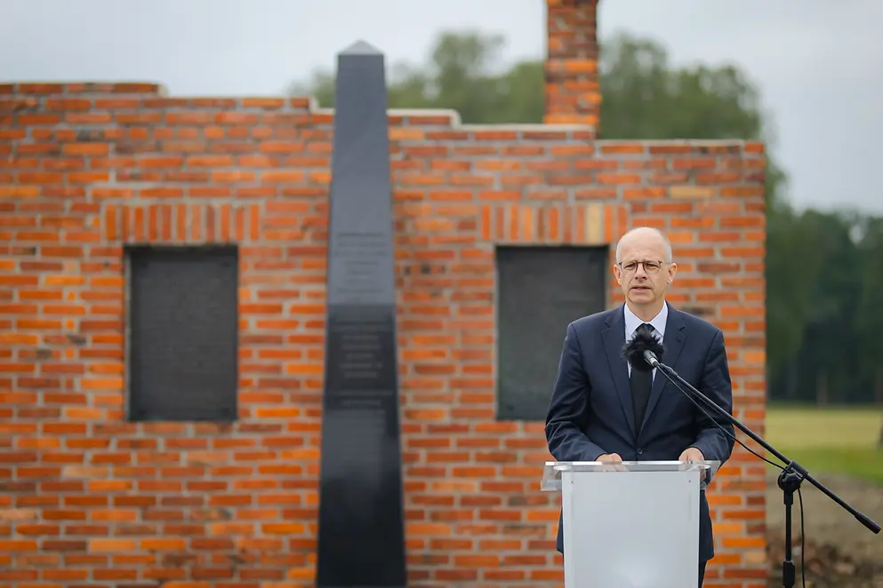 Michael Brand steht vor einem Rednerpult unter freiem Himmel vor einer Mauer
