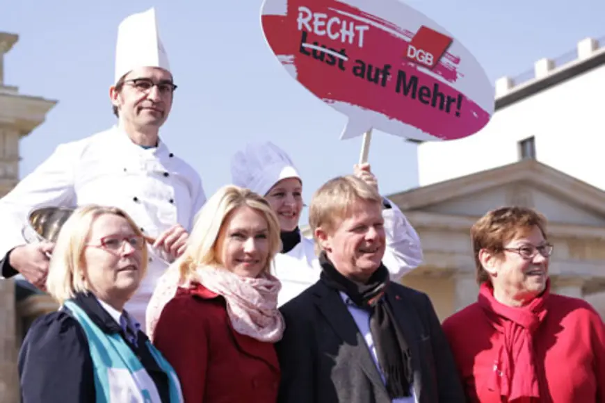 Manuela Schwesig und Reiner Hoffmann in einer Gruppe Menschen, zwei davon als Köche verkleidet