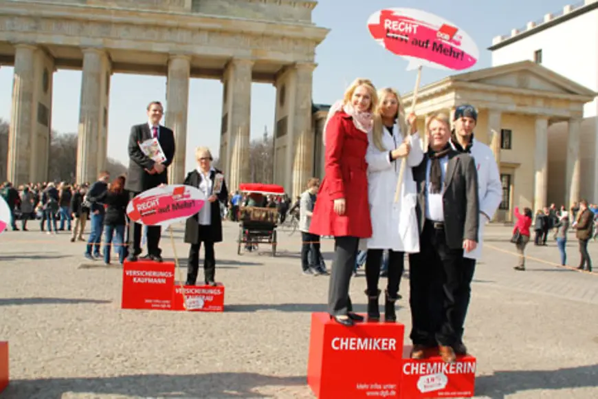 Manuela Schwesig stehtgemeinsam mit Reiner Hoffmann und zwei weiteren Personen auf einem Treppchen